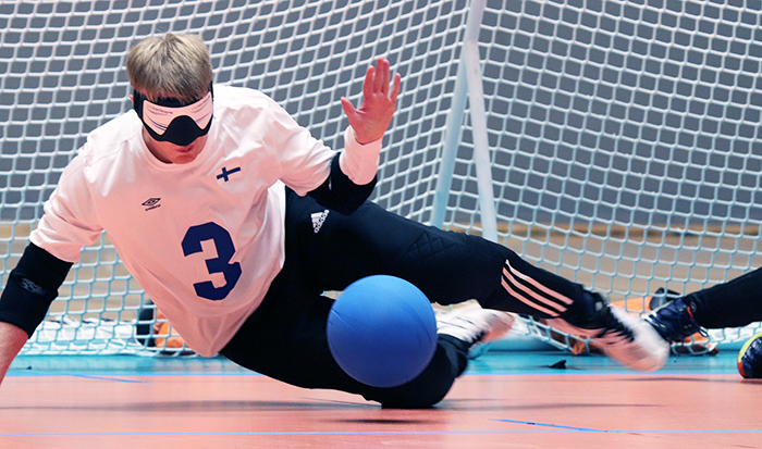 Kuvassa Eetu Eronen valkoisessa suomi-paidassa numerolla 3. Eetu on juuri torjumassa palloa. Pallo on kuvan etulaidassa tulossa kohti Eetun jalkoja.
